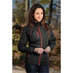 A woman wearing a black thermal jacket with red accents, standing outdoors in a natural setting. The jacket has a logo.