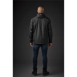 A man wearing a black rain jacket, viewed from the back, paired with dark jeans and shoes. The jacket has a hood and logo.