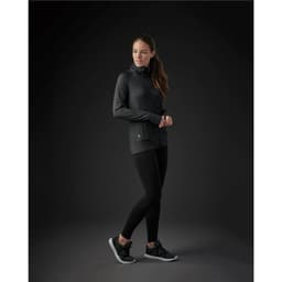 A woman in a black zip-up jacket poses with a sleek silhouette, paired with black leggings and sporty shoes.
