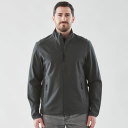 A man wearing a dark grey softshell jacket with a zip front and side pockets. The jacket has a logo.