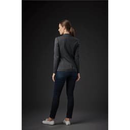A woman wearing a dark grey knit blazer, paired with dark jeans and white shoes, facing away from the viewer.