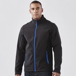 A man wearing a black softshell jacket with blue accents and zippered pockets, featuring a logo.