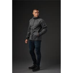 A model wearing a grey men's softshell jacket, paired with dark jeans and black shoes, standing against a dark background.