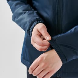 A navy thermal jacket featuring elastic cuffs, with a person's hand adjusting the sleeve. The jacket has a logo.