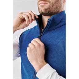 A blue men's vest with a high collar, featuring a zippered front closure and a model adjusting the zipper.