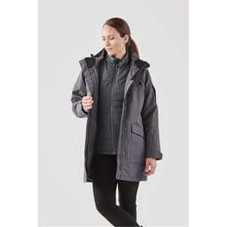 A grey women's 5-in-1 system jacket featuring a hood and multiple pockets, modelled by a woman.