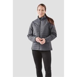 A woman wearing a grey insulated jacket with a zip front and stands against a light background.
