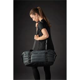 A grey quilted duffle bag with adjustable straps, being carried by a person in athletic wear.