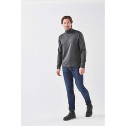 A man wearing a charcoal grey 1/4 zip long sleeve shirt paired with jeans and boots, standing against a neutral background.