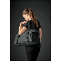 A woman carrying a large black duffle bag over her shoulder. The bag has a logo and adjustable straps.