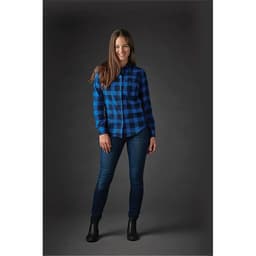 A woman wearing a blue and black checked button-up shirt and jeans, featuring a logo on the shirt.