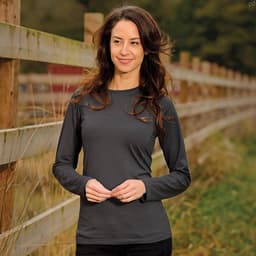 A woman models a long-sleeve, charcoal grey tee with a simple design, set against a natural outdoor backdrop.