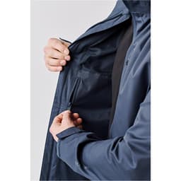 A person holding the zipper of a navy blue lightweight rain jacket with an interior pocket. The jacket has a logo.