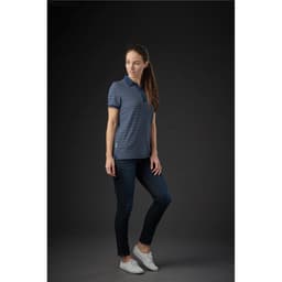 A woman wearing a navy and white striped polo shirt with a logo, paired with jeans and white shoes.
