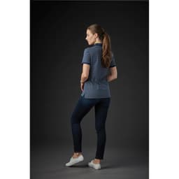 A woman in a navy and white striped polo shirt stands with her back to the camera, paired with dark jeans and white shoes.