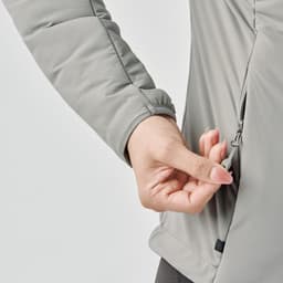 A hand adjusting the zipper of a light grey women's puffer jacket, featuring a sleek design and logo.