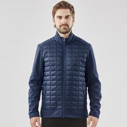 A men's softshell jacket in navy blue featuring a quilted front and zippered pockets. The jacket includes a logo.