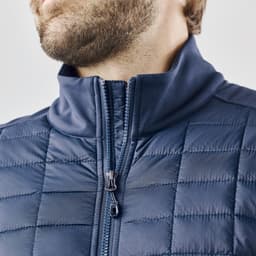 A men's softshell jacket in navy blue with a high collar and quilted texture. Features a zippered front.