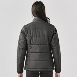 A women's puffer jacket in dark grey, featuring a quilted design and a high collar. It includes a logo on the back.
