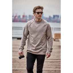 A man wearing a beige crew neck fleece sweater and sunglasses, holding a camera while walking on a pier.