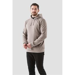 A man in a beige fleece pullover hoodie stands against a plain background, hands clasped. The hoodie features a logo.