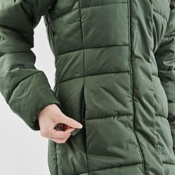 A green women's puffer jacket with a zipper pocket and quilted texture, featuring a person’s hand interacting with it.