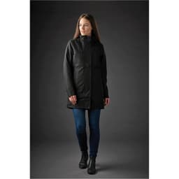 A woman models a long, black Montauk System Jacket, featuring a high collar and a fitted silhouette.
