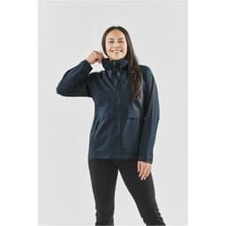 A woman wearing a navy blue technical shell jacket with a zip-up front and high collar, featuring a logo.