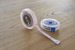 A plastic retractable tape measure in clear casing with a white measuring tape, sitting on a wooden surface.