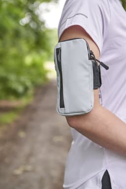 A grey armband featuring a zippered pocket, worn on a person's upper arm, set against a natural background.