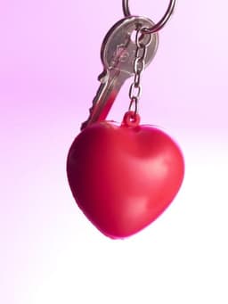 A red heart-shaped PU foam key holder attached to a key, with a soft pink background.