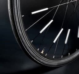 A bicycle wheel featuring several white ABS reflective strips attached to the spokes. The background is dark.