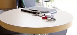 A round table featuring a notebook, pens, keys, and a tin of mints in various colours.