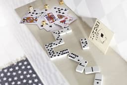 A wooden box containing a game set with white dominoes, playing cards, and dice scattered on a light-coloured surface.