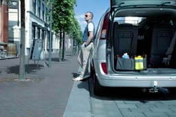 A grey polyester car organiser is placed in the boot of a silver car, featuring various bottles and containers.