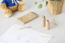 A wooden tube containing coloured pencils in various shades, alongside a notebook, sketches, and a teddy bear.
