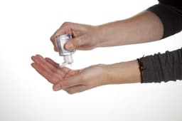 A clear hand cleansing gel being dispensed from a small bottle into a hand, with a neutral background.