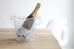 A clear ice bucket with a bottle of champagne inside, surrounded by ice cubes on a wooden table.