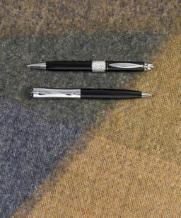 A black metal ballpen featuring a silver accent and a shiny silver clip, displayed on a textured background.