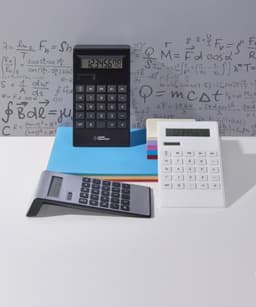 A black, silver, and white calculator trio sits atop coloured papers with mathematical equations in the background.