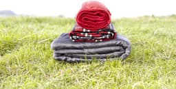 Three rolled polyester blankets in red, black and grey stacked on green grass.