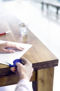A blue PS letter opener being used on a sheet of white paper on a wooden table.