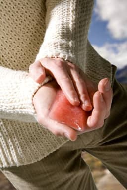 A person holding a pink PVC self-heating pad in their hands, wearing a cream-coloured knitted sweater.