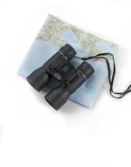 Black plastic binoculars with a neck strap, resting on a folded map. The binoculars have a logo.