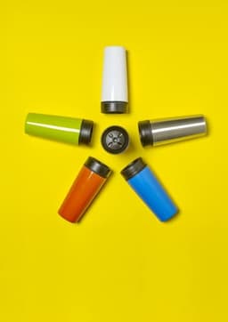 A collection of stainless steel double-walled travel mugs in green, white, orange, blue, and silver, arranged in a star shape.