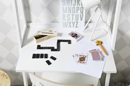 A wooden box labelled “DOMINO” sits on a white desk with black dominoes and playing cards scattered around.
