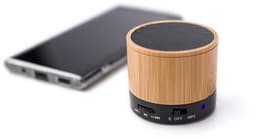 A bamboo wireless speaker with a black base and buttons, positioned next to a smartphone.