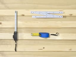 A blue PE tape measure and two white measuring tapes on a wooden surface. The image features a logo on the tape measure.