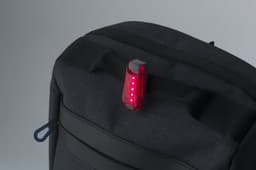 A red ABS safety light attached to a dark fabric backpack. The light features multiple LED indicators.