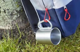 A stainless steel double-walled mug hangs from a bag, featuring a shiny metallic finish and a simple design.